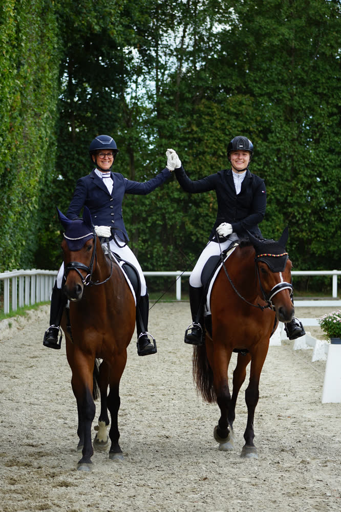 Carolin Schnigula auf Romeo HB und Sarah Philine Koch auf My Milou reiten nebeneinander im Viereck und schlagen sich zur Begrüßung die Hände ein